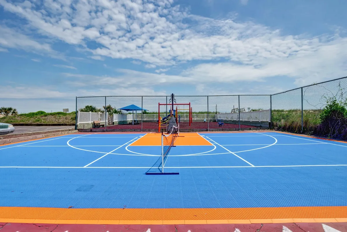 This image captures a bright outdoor court with a basketball hoop and tennis net set against a colorful surface. The open sky and welcoming, playful design invite guests to engage in recreational activities and group fun.