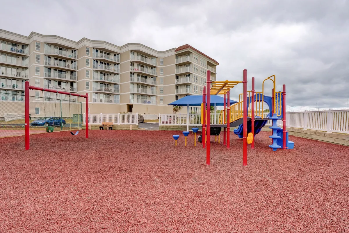 A cheerful outdoor playground with swings and playground equipment, surrounded by nearby buildings. The area is bustling with children playing and families gathering, radiating joy and energy.