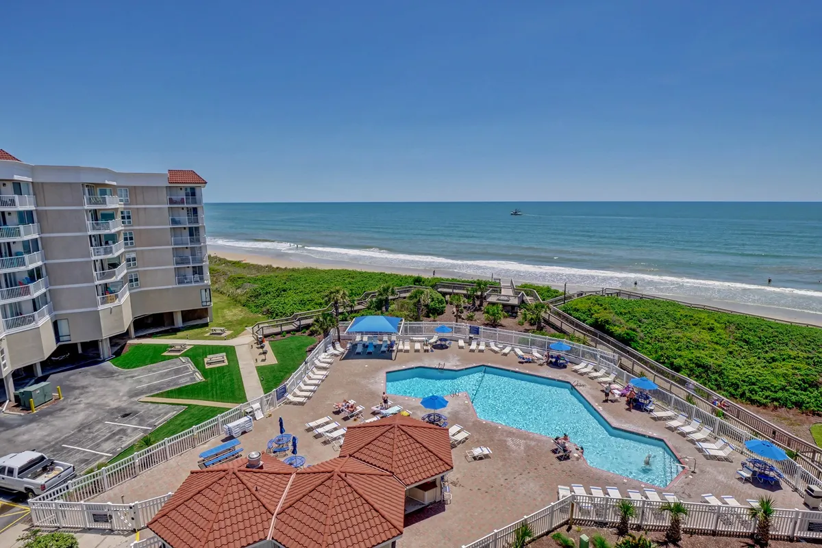 The hero image captures a stunning exterior view of the condo's brand new saltwater covered pool, surrounded by lush landscaped gardens, with the Atlantic Ocean sparkling in the background. Poolside cabanas invite relaxation, while the beach stretches just steps beyond, promising endless opportunities for sunbathing, swimming, and seaside strolls. The tranquil, vacation-like atmosphere is perfect for families or couples seeking a serene coastal retreat.