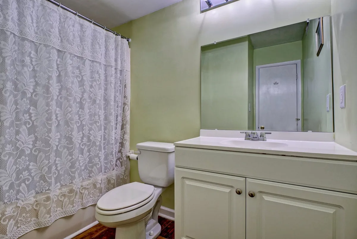 A serene bathroom featuring a vanity with mirror, toilet, and shower curtain. The space is calm and functional, ideal for personal grooming and refreshing after a day at the beach.