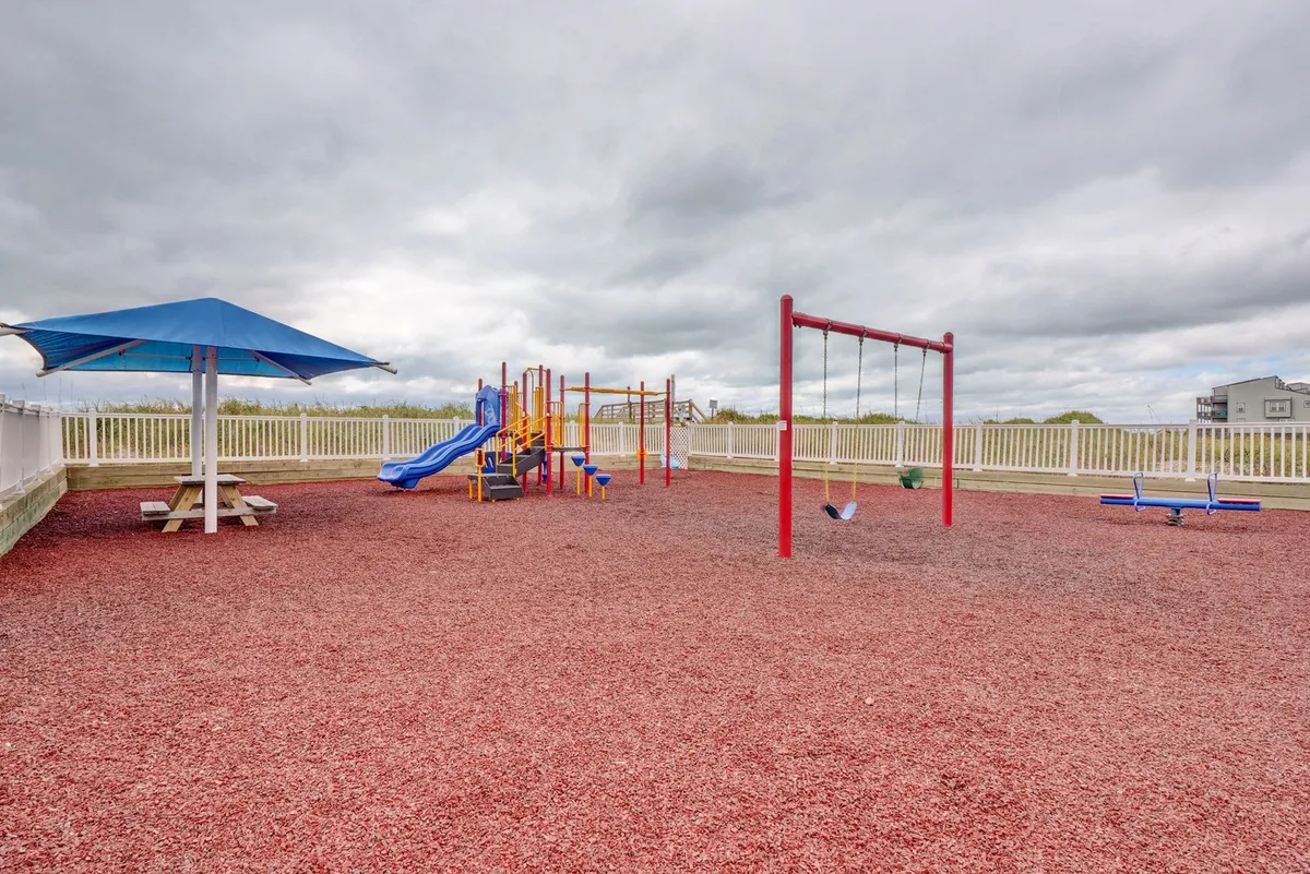 A cheerful outdoor playground featuring modern play equipment, swings, a picnic table, and a shade structure, with children playing and families enjoying time together. The setting is bright and safe, epitomizing family fun and connection.