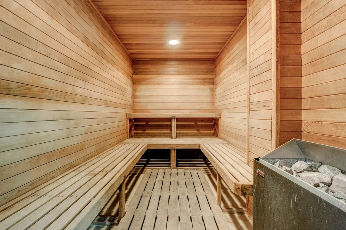 A tranquil, wood-paneled sauna with stone heater and wooden benches, inviting guests to relax, unwind, and enjoy a wellness retreat within steps of their condo. The warm lighting and natural materials evoke a spa-like experience.