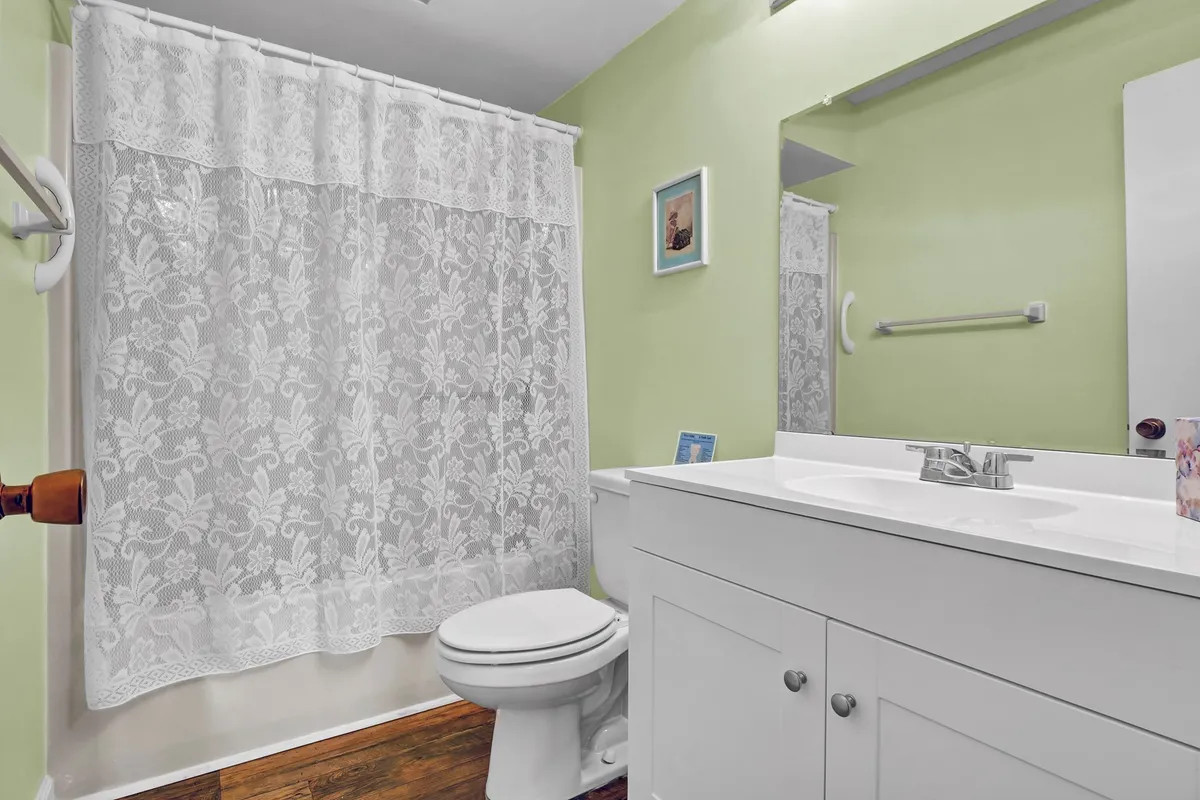 An inviting bathroom with a white lace shower curtain, vanity with sink, and a mirror. The space feels clean, welcoming, and well-maintained, supporting a relaxing bath or morning routine.