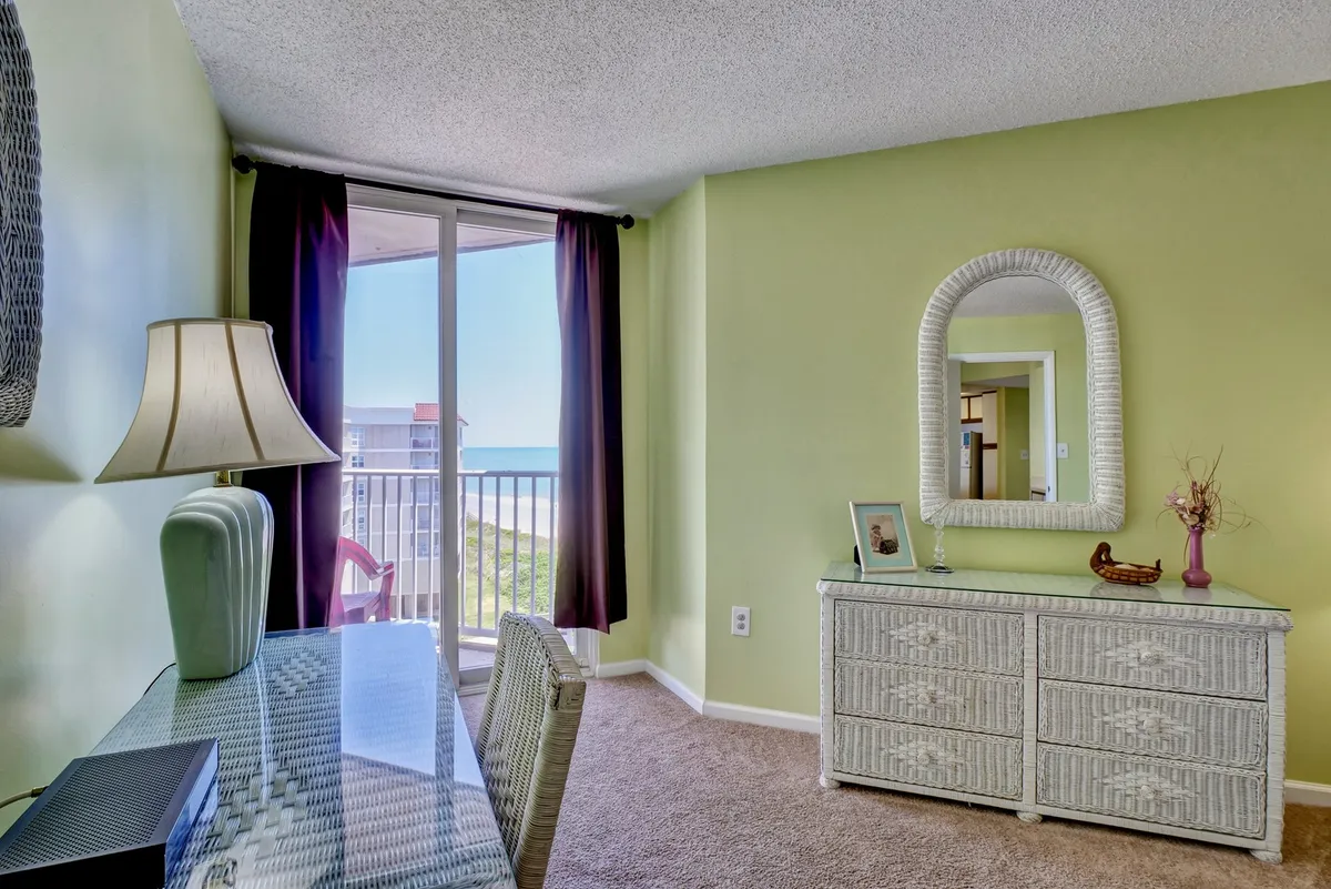 A tranquil interior space with a window offering panoramic ocean views, a dresser with mirror, and a desk with lamp. The setting is bright and fresh, ideal for working or unwinding while enjoying the sea breeze and natural light.