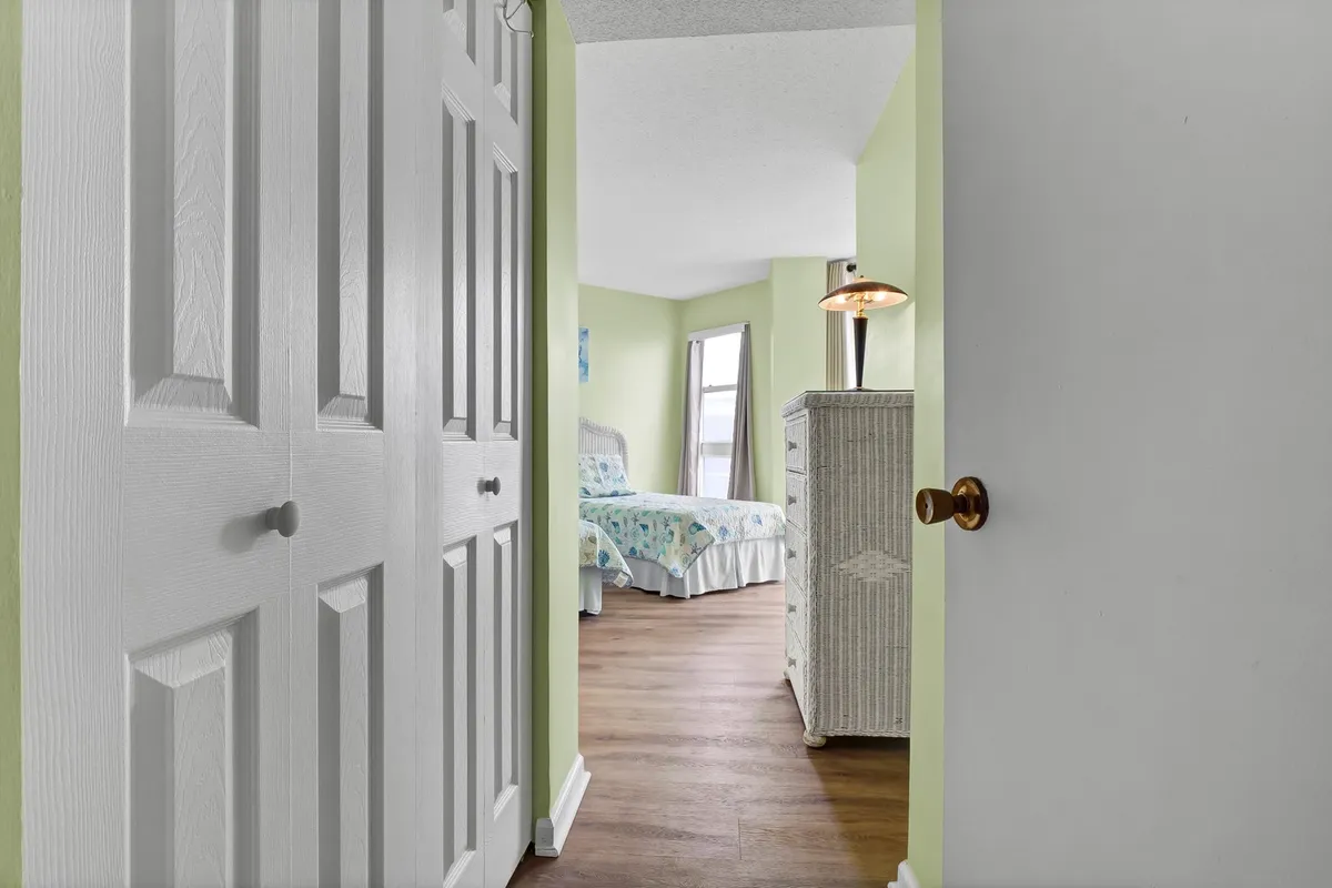 A calm queen bedroom with closet doors, a dresser, a cozy bed, and a window with curtains letting in natural light. The space feels peaceful, welcoming, and sunlit, ideal for relaxation and restful sleep.